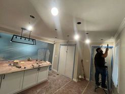 Person painting a room, with kitchen island and cabinet doors.