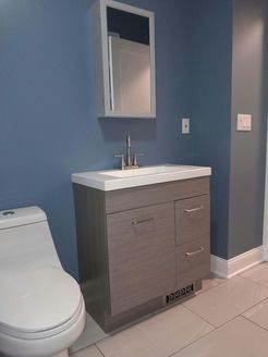 Bathroom with a gray vanity, white countertop, and blue wall; toilet on the left, mirror above.