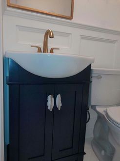 Navy blue bathroom vanity with a white sink, gold faucet, and a toilet.