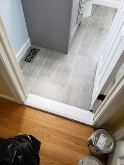 Bathroom doorway with wood floor leading to tiled bathroom. Paint cans and trash in foreground.