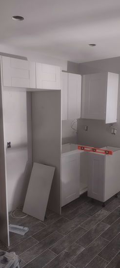 Kitchen renovation with white cabinets, light gray walls, and dark gray tile flooring.