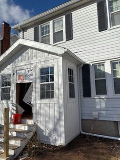 White house with a small, enclosed porch and black shutters. A red bucket sits on the porch steps.
