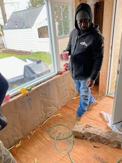 Man in jacket and jeans inside a building under construction, holding a cup.