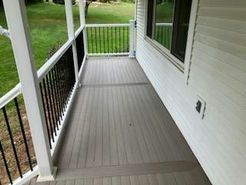 Grey composite deck with black railing and white pillars, next to a white house with windows.