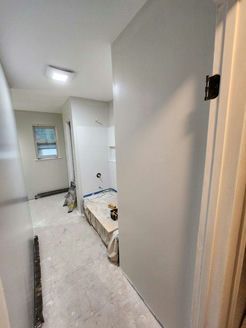 Narrow hallway with light gray walls, leading to a bathroom; construction in progress.