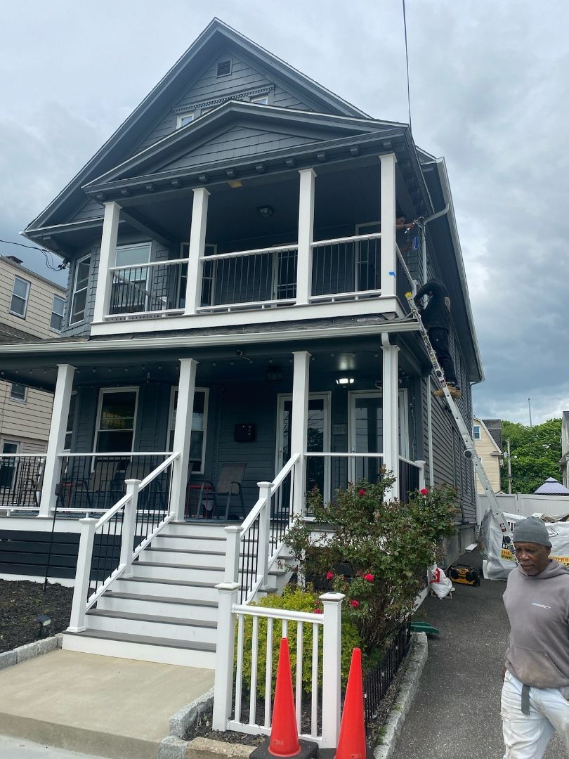 Two-story gray house with white porch, stairs, and a man walking by.