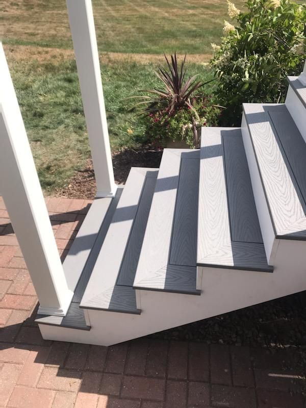Outdoor staircase with gray and white composite steps, leading to a porch with white pillars.