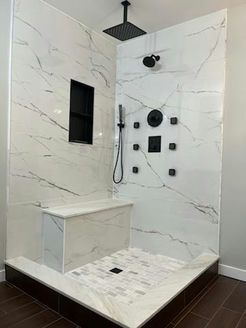 Modern white and gray tiled shower with black fixtures and built-in bench.
