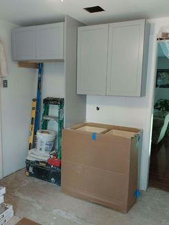 Cabinets being installed in a room under construction, with tools and a cardboard box present.