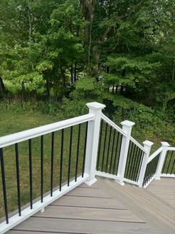 Wooden deck with white railings and black spindles, overlooking a green yard and trees.