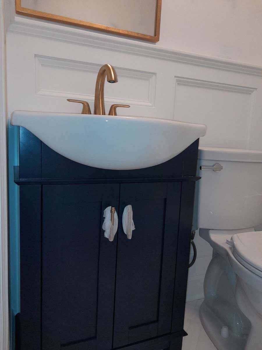 Navy blue bathroom vanity with a white sink, gold faucet, and two white towel holders.