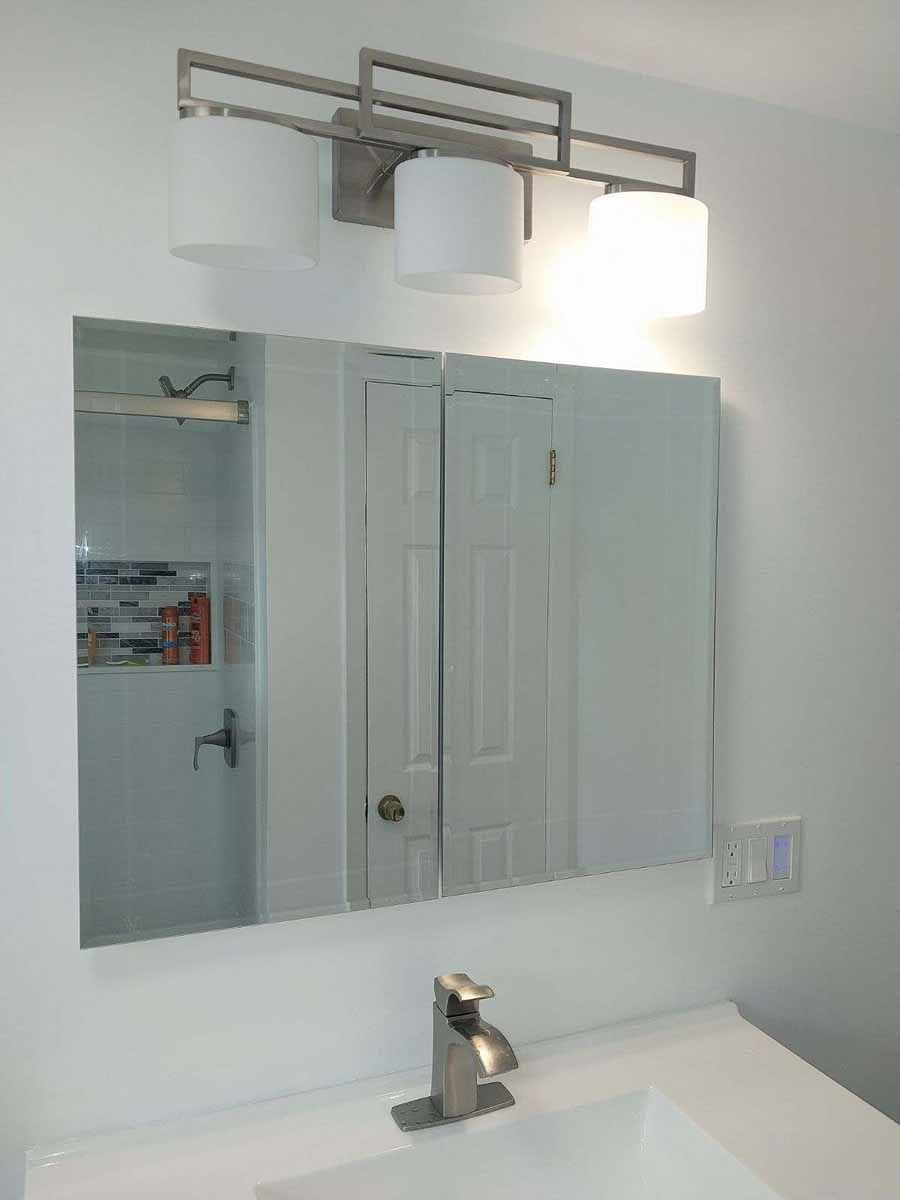 Bathroom with a mirror, light fixture, sink, and cabinet against a white wall.