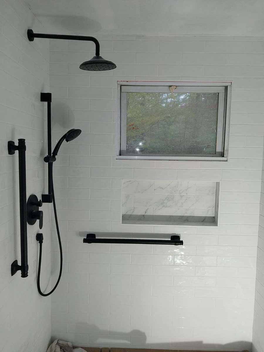 Black shower fixtures against white tiled wall with a small window and a recessed shelf.