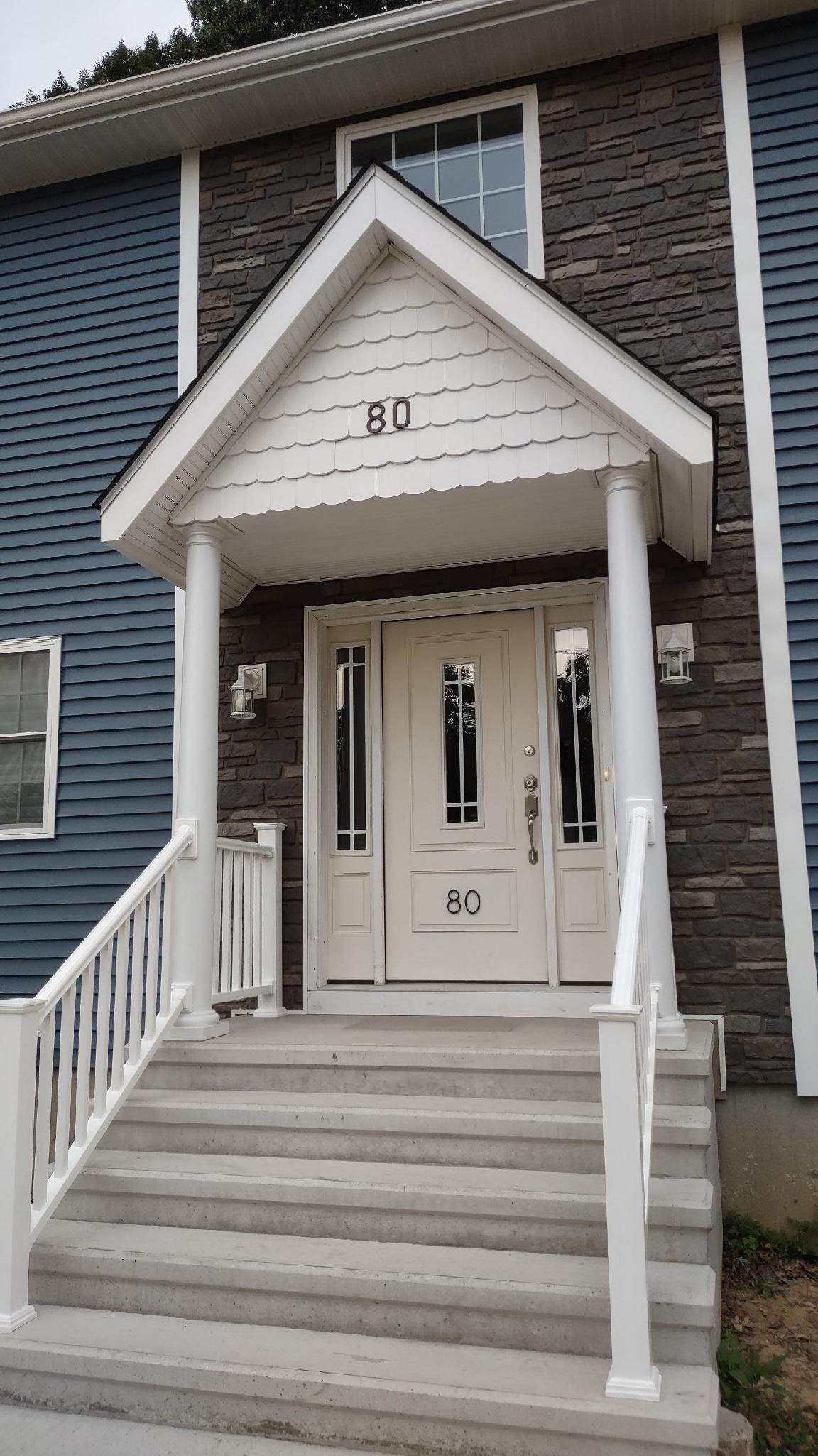 White-doored entrance to a building with steps and a small roofed overhang; blue and stone-colored siding.