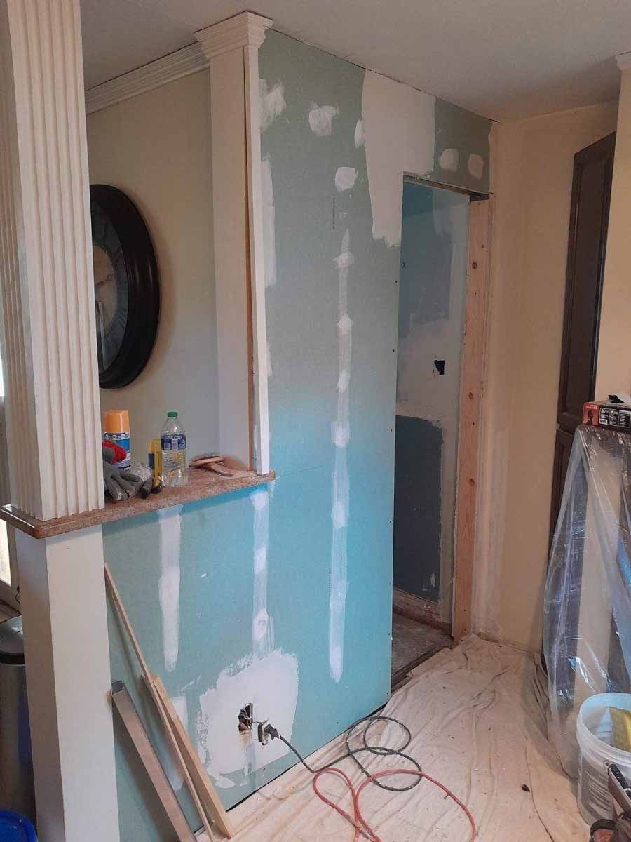 Interior renovation: Drywall installed, unfinished doorway, electrical wires visible.