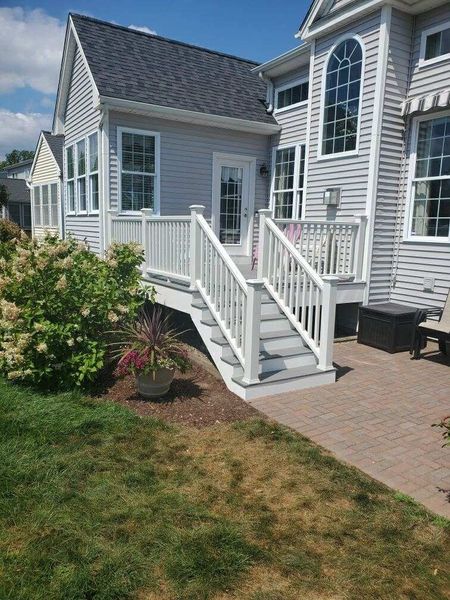 Back deck with stairs, white railing, leading to a house with gray siding.