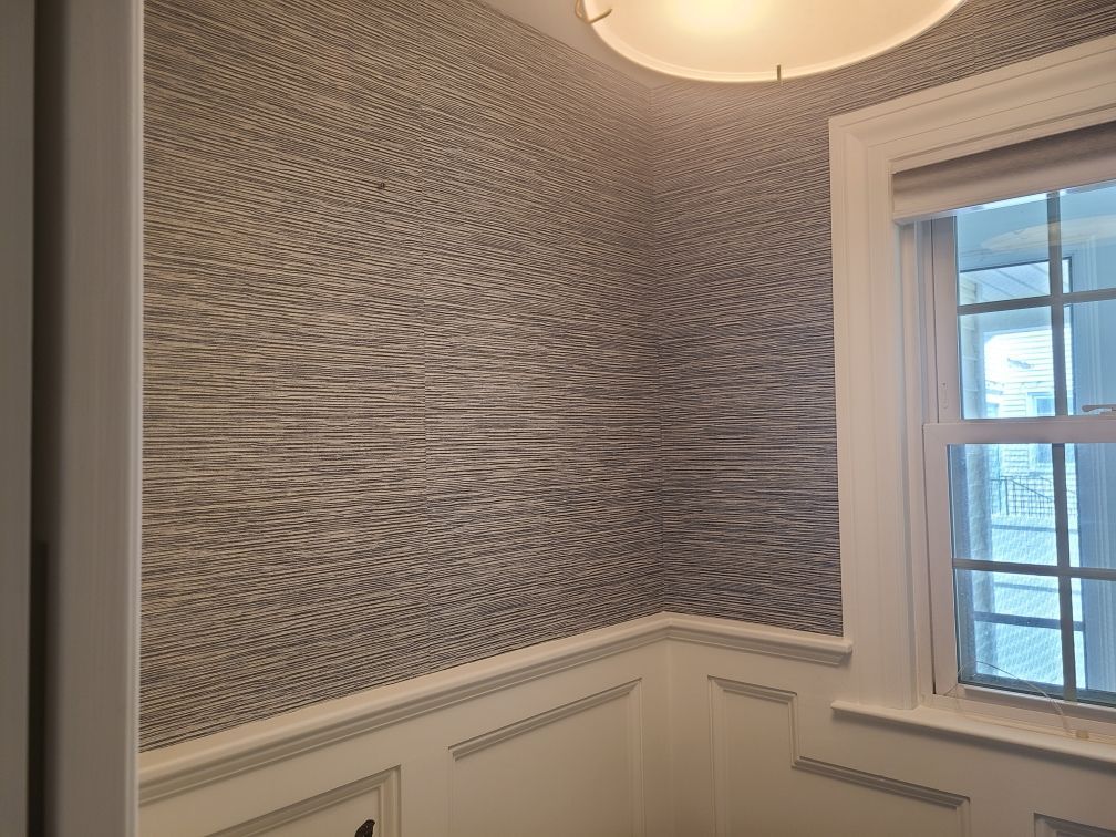 Room corner with textured wallpaper, white trim, and a window with a light fixture above.