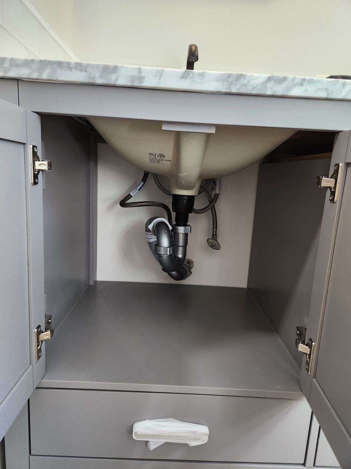 Gray bathroom vanity cabinet with open doors, showing plumbing under a white sink.