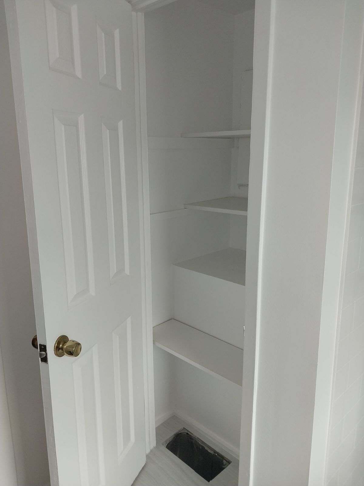 White closet with shelves and door slightly open, a/c vent at base.