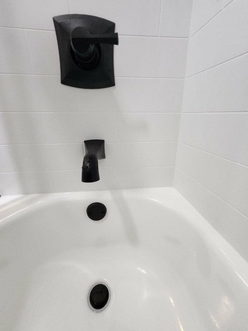 Black tub faucet and handle on white tiled wall. Tub is white.