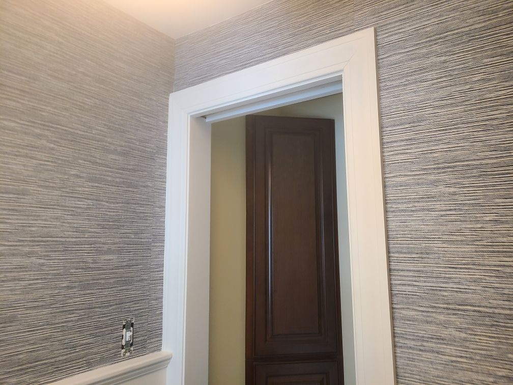 Doorway with white trim, gray textured wallpaper. Doorway leads to a dark brown cabinet.