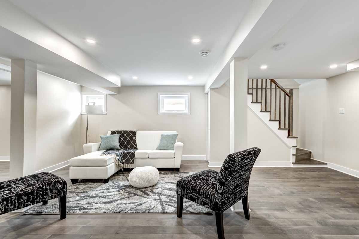 Modern basement living room with a white sectional sofa, patterned chair, and stairs.