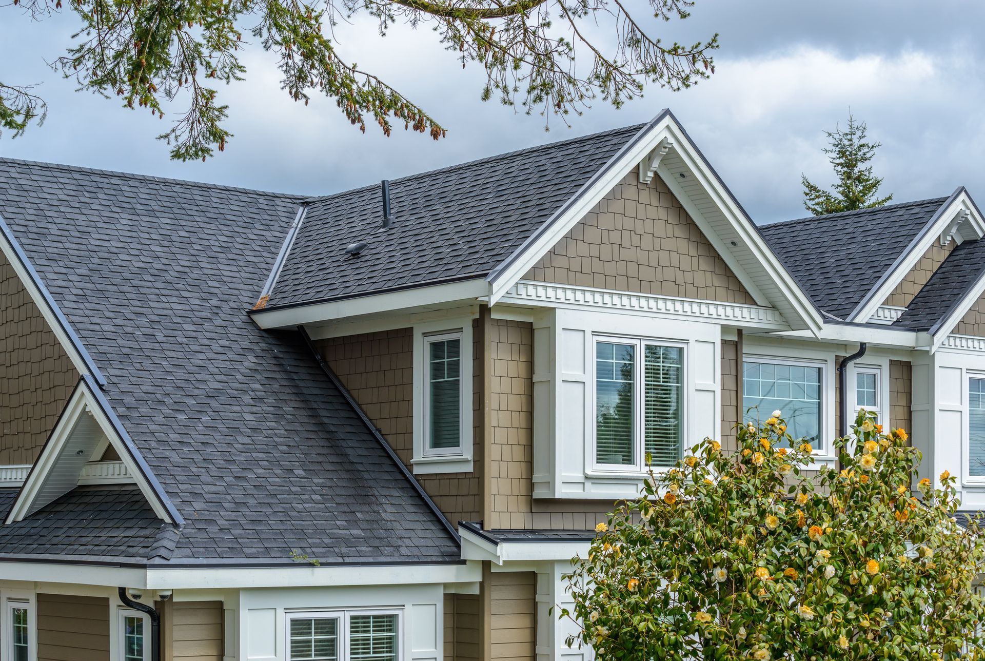 Brown house with dark gray shingle roof, white trim, and a cloudy sky.