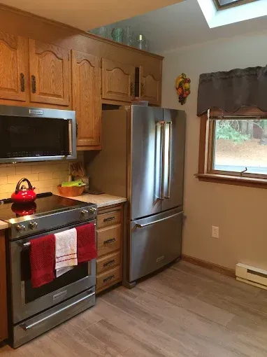 Kitchen with wood cabinets, stainless steel appliances, and a window with a gray valance.