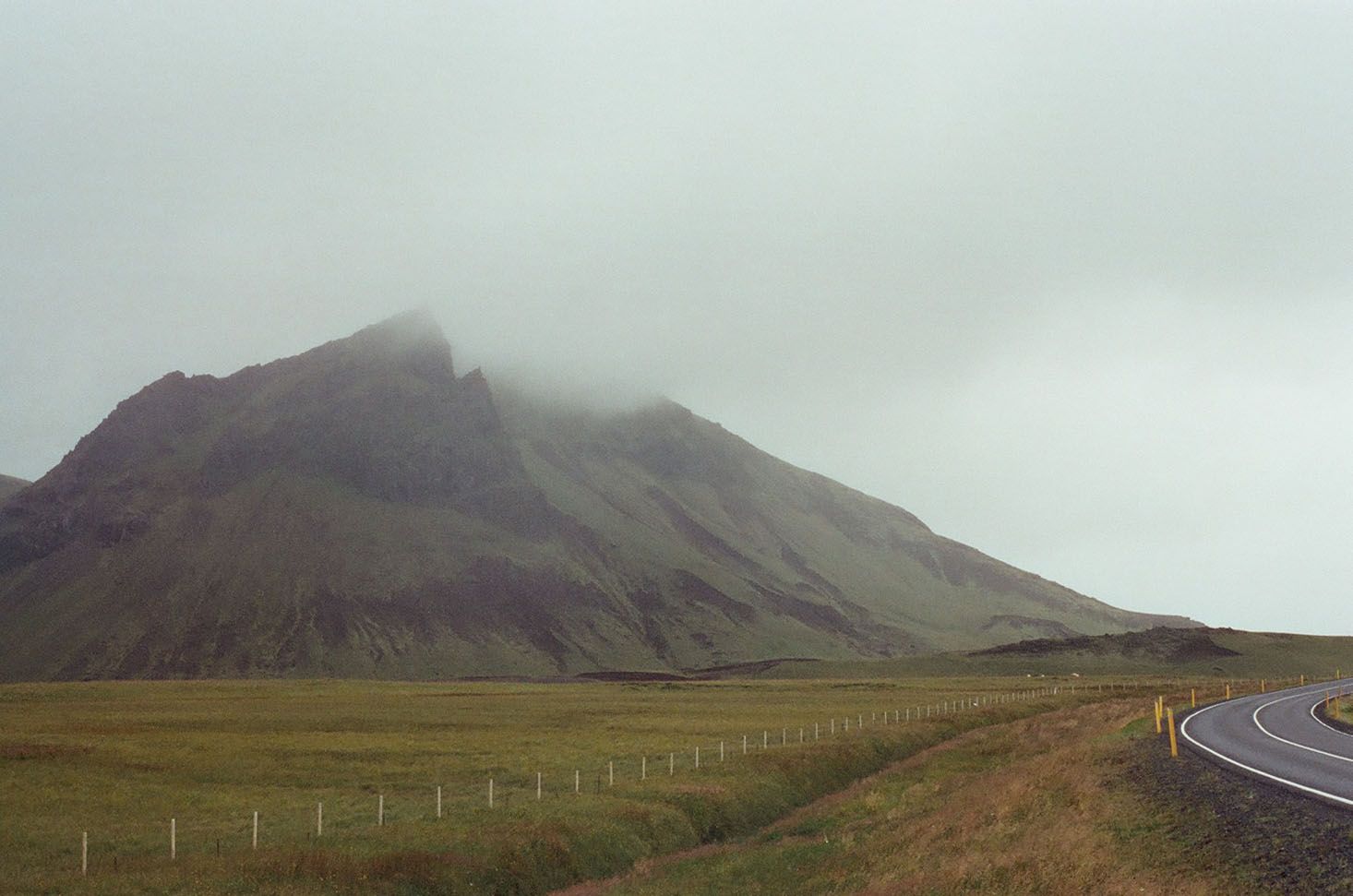 Mist-covered mountain beside a winding road in a grassy landscape