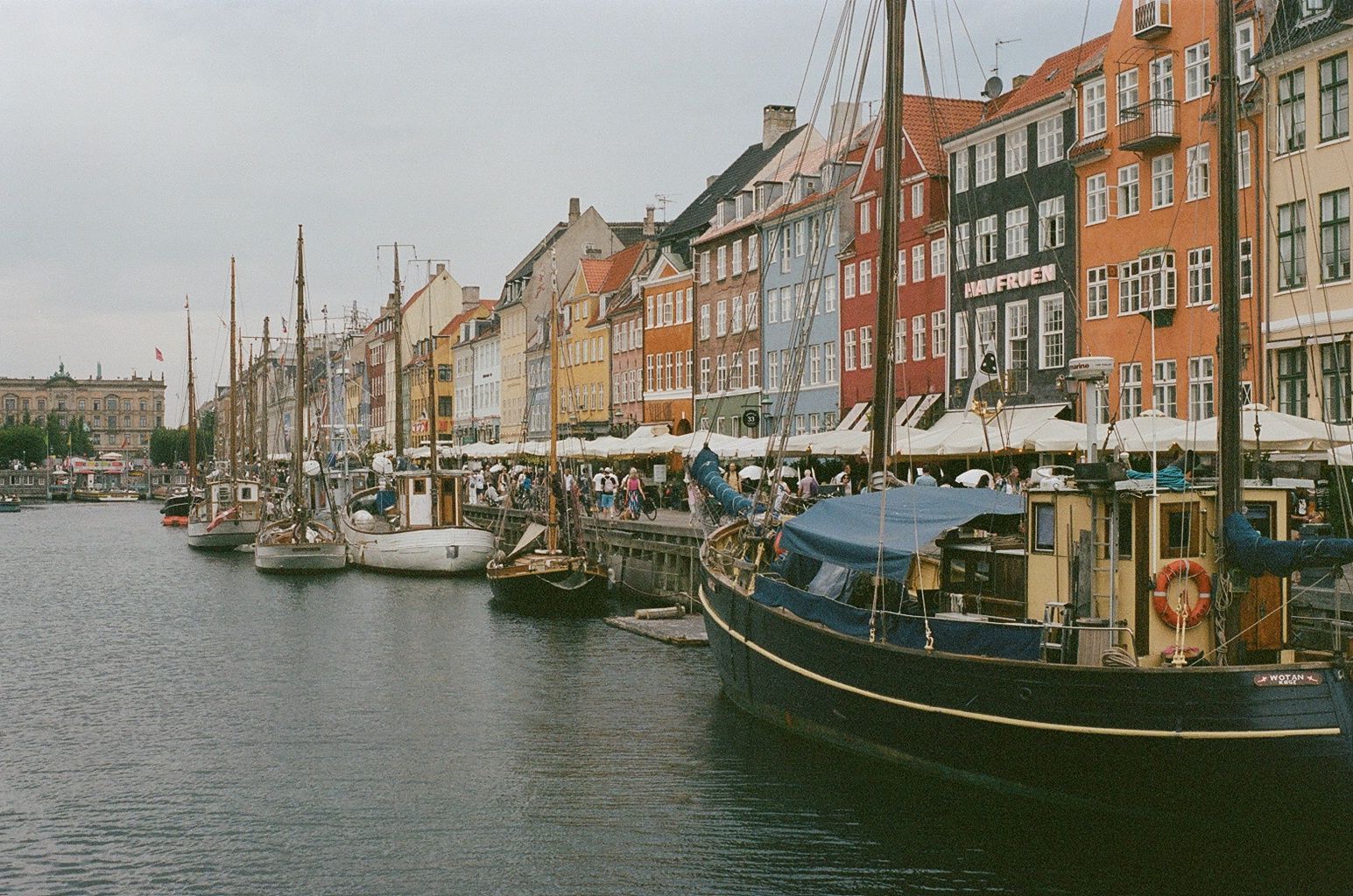 Canal with moored boats beside colorful waterfront buildings on a cloudy day
