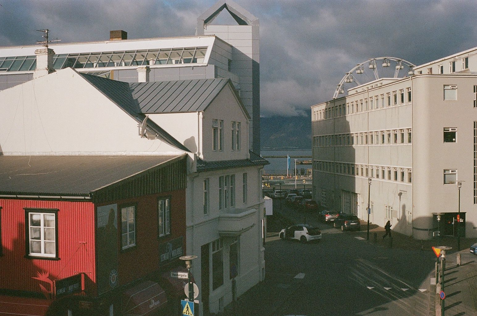 Narrow street between white buildings under cloudy sky, with a red house in the foreground.