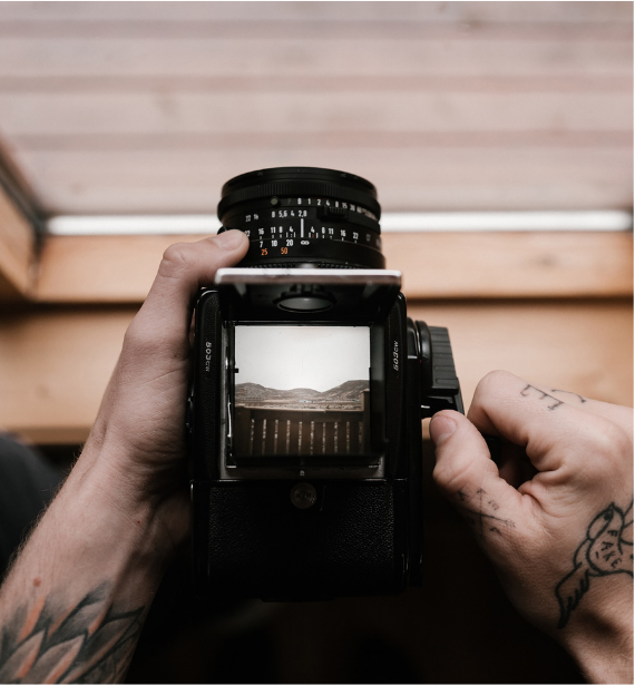 Hands adjusting a vintage camera viewfinder with a landscape framed inside.