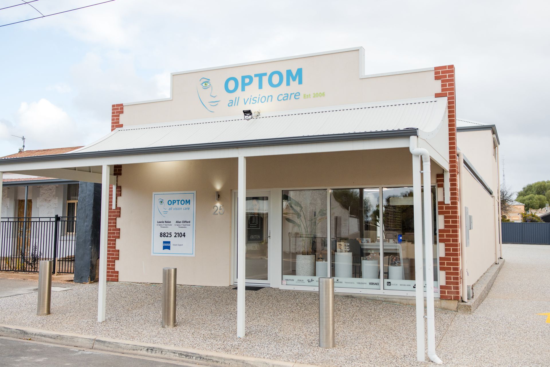 Optometrist storefront with glass entrance and white facade under a cloudy sky