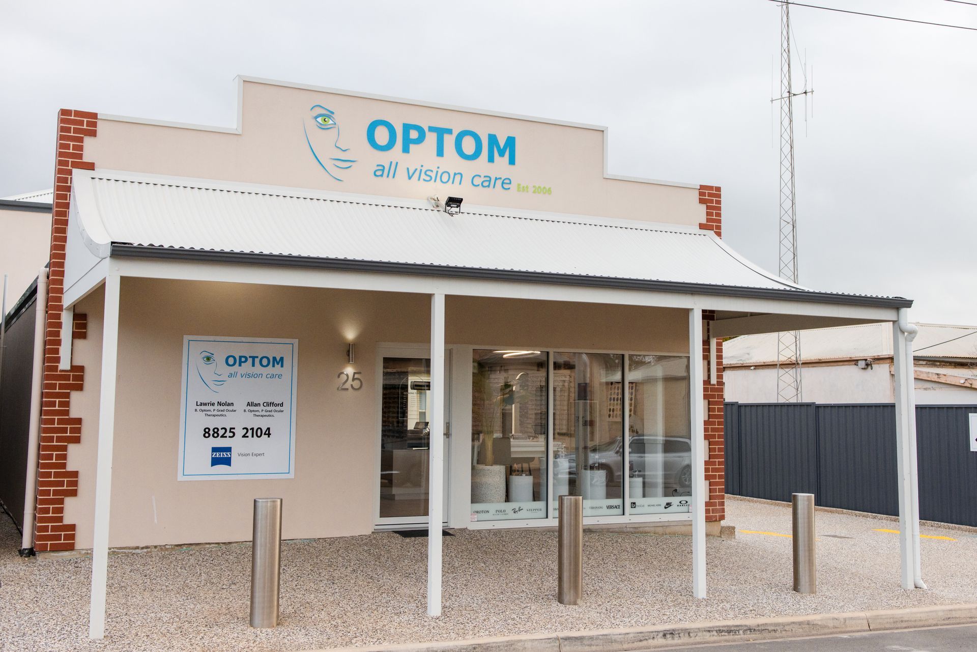 OPTOM eyecare storefront with beige facade, glass entrance, and parking bollards under a white awning