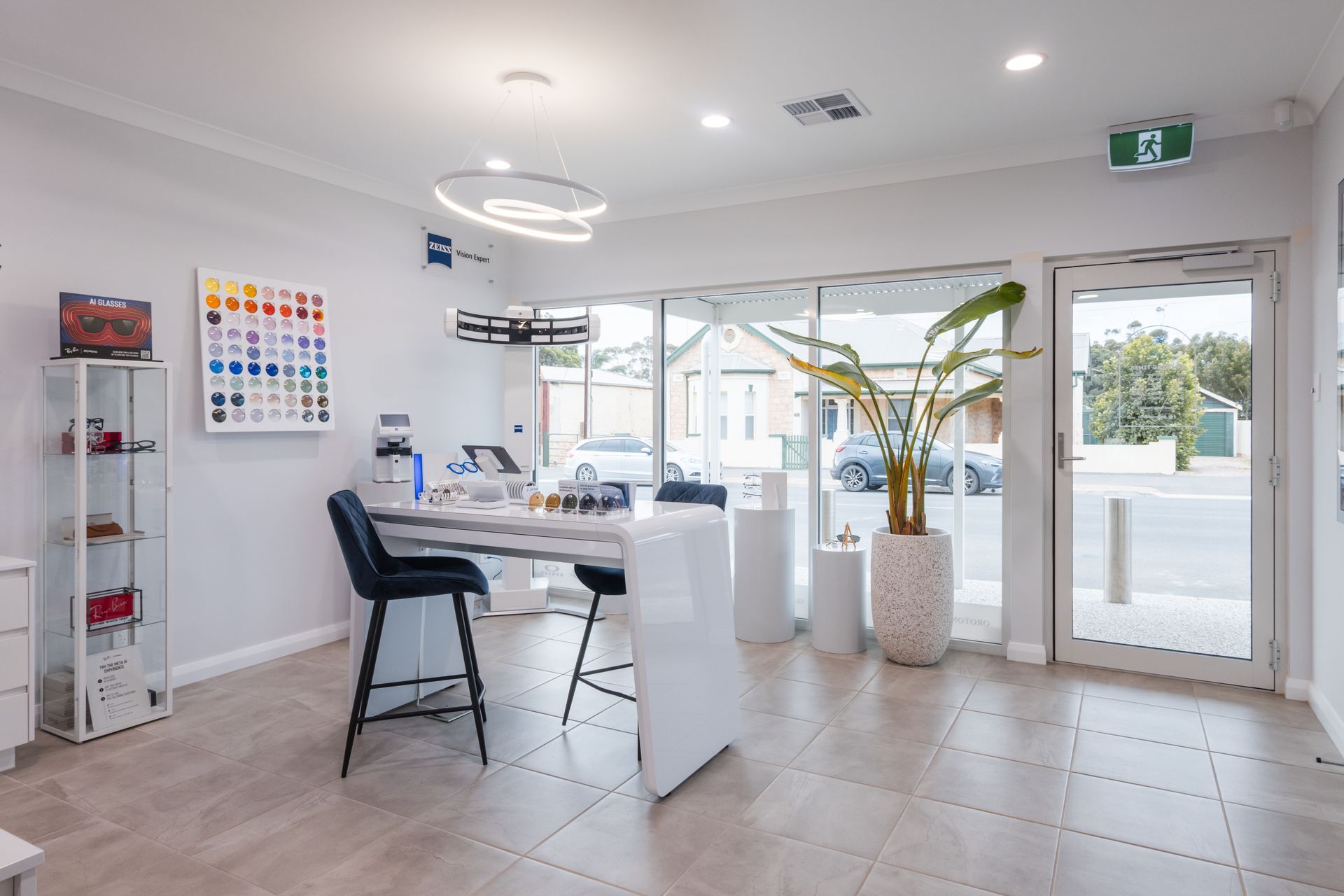 Bright modern office with white desk, black chair, plants, and large glass doors overlooking outside.