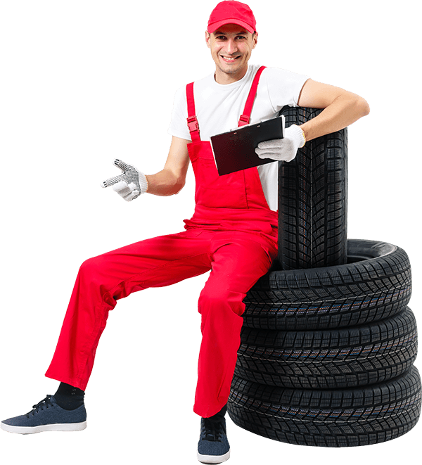 A man in red overalls is sitting on a pile of tires holding a tablet.
