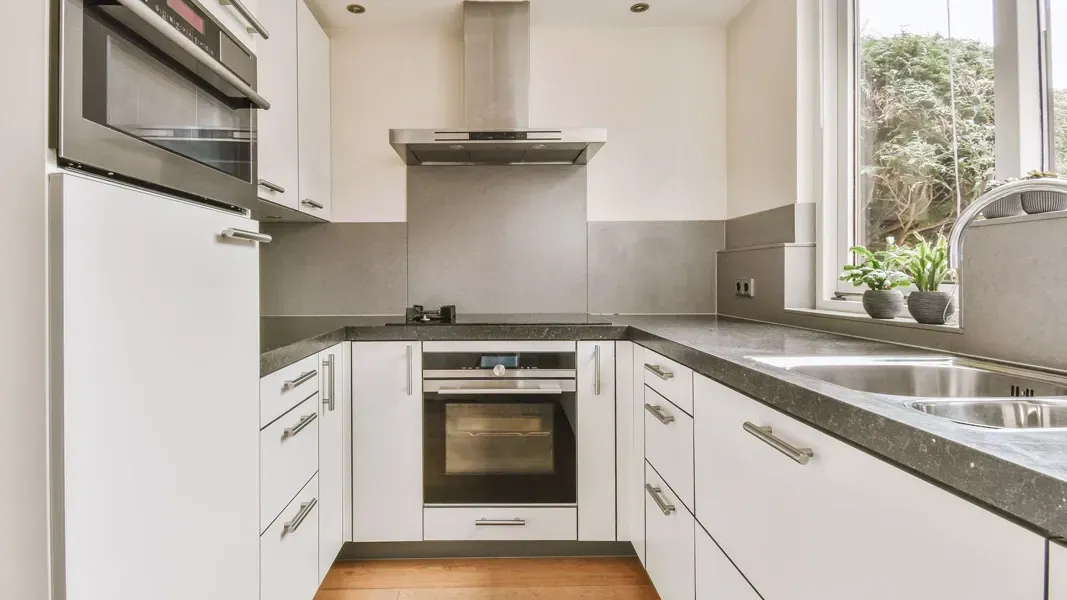 A kitchen with white cabinets , stainless steel appliances , a sink , and a window.