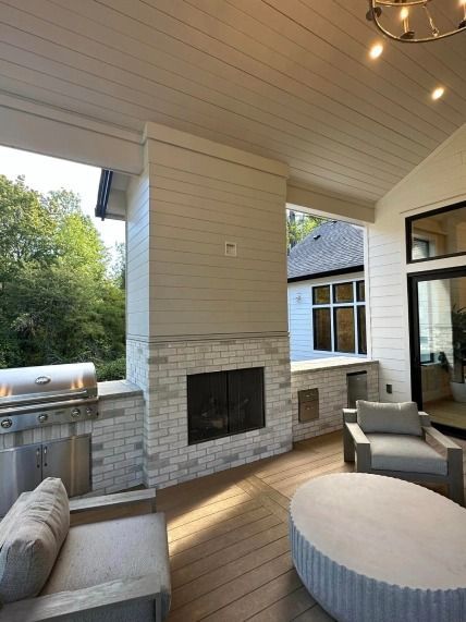 A patio with a fireplace , chairs , a table and a grill.
