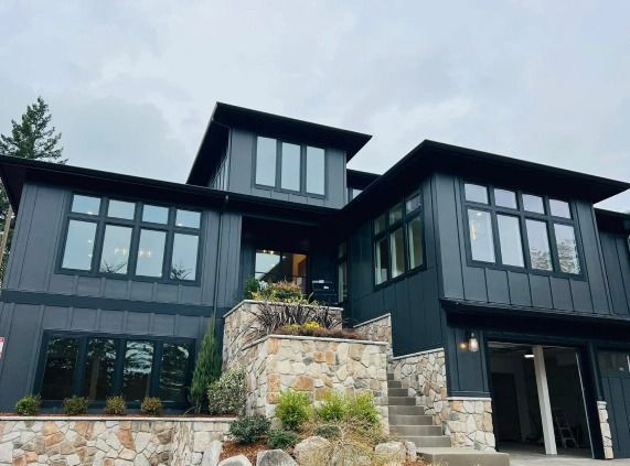 A large black house with a lot of windows is sitting on top of a hill.