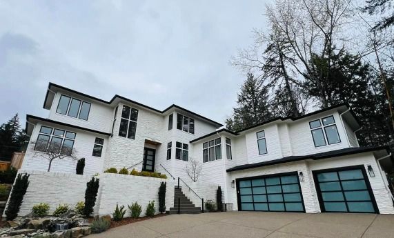 A large white house with two garages and trees in the background.