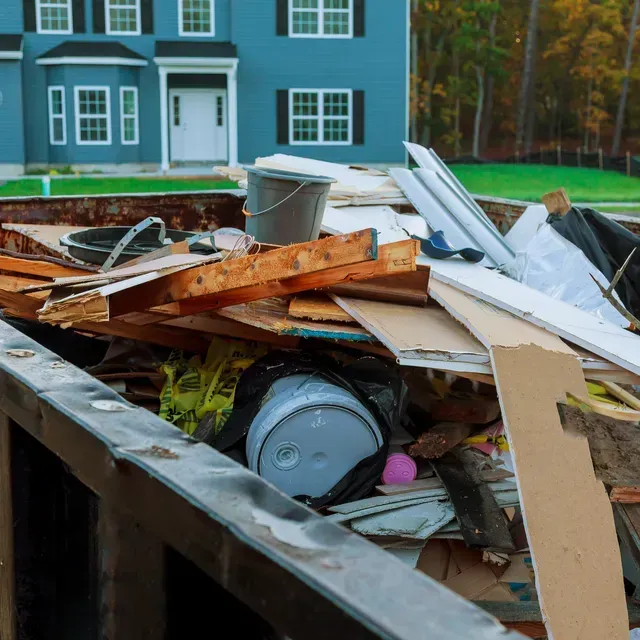 A dumpster filled with junk in front of a blue house