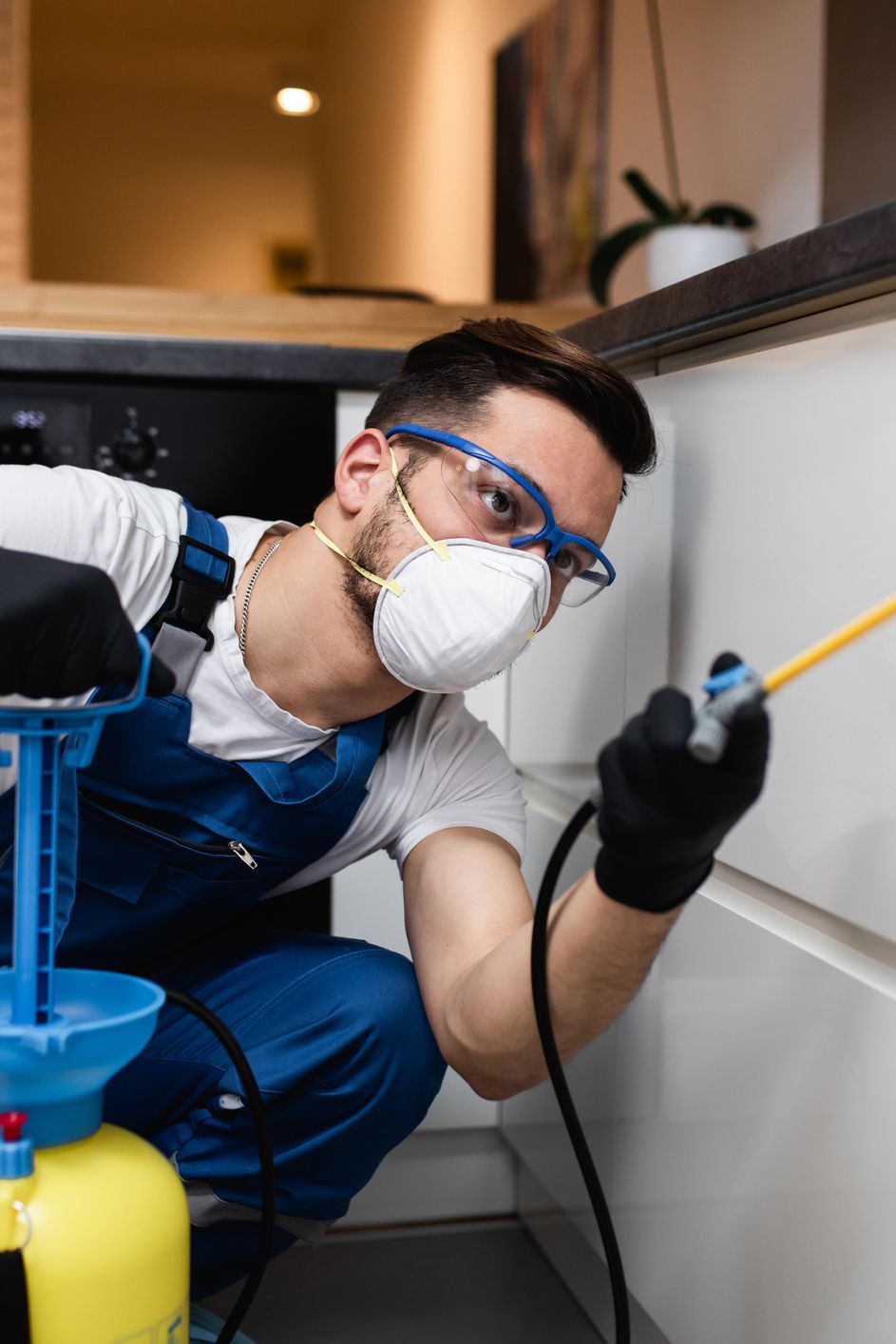 Pest control worker spraying insecticide in a kitchen, wearing protective gear.