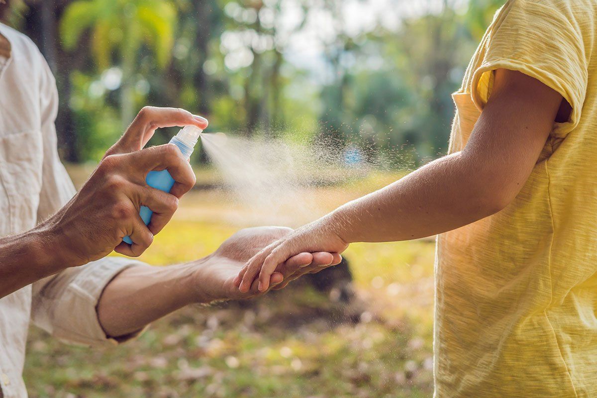 Person spraying insect repellent on another person's arm outside.
