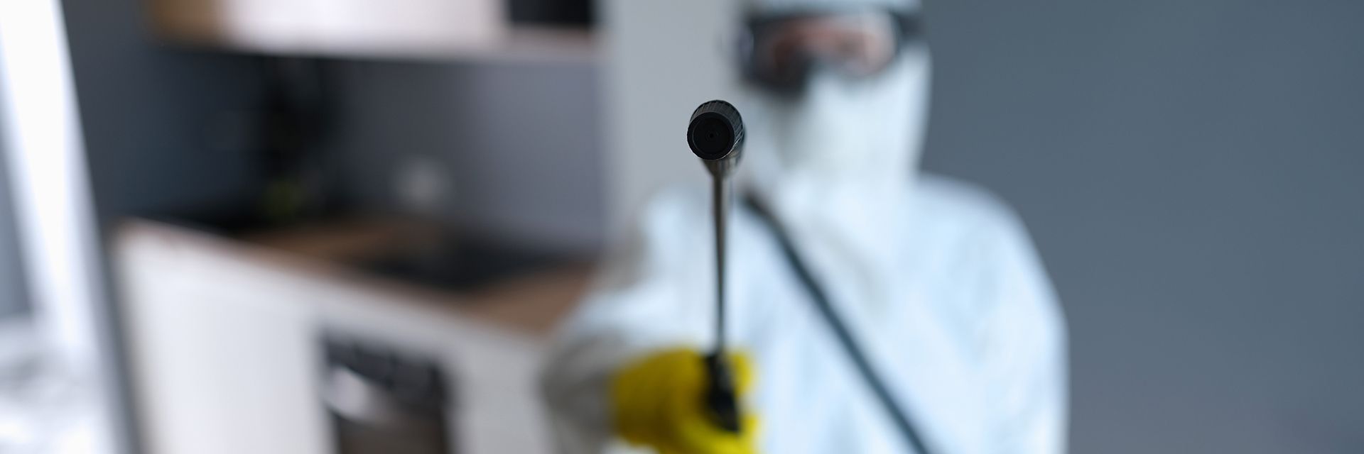 Person in protective suit aiming a spray wand forward inside a room.
