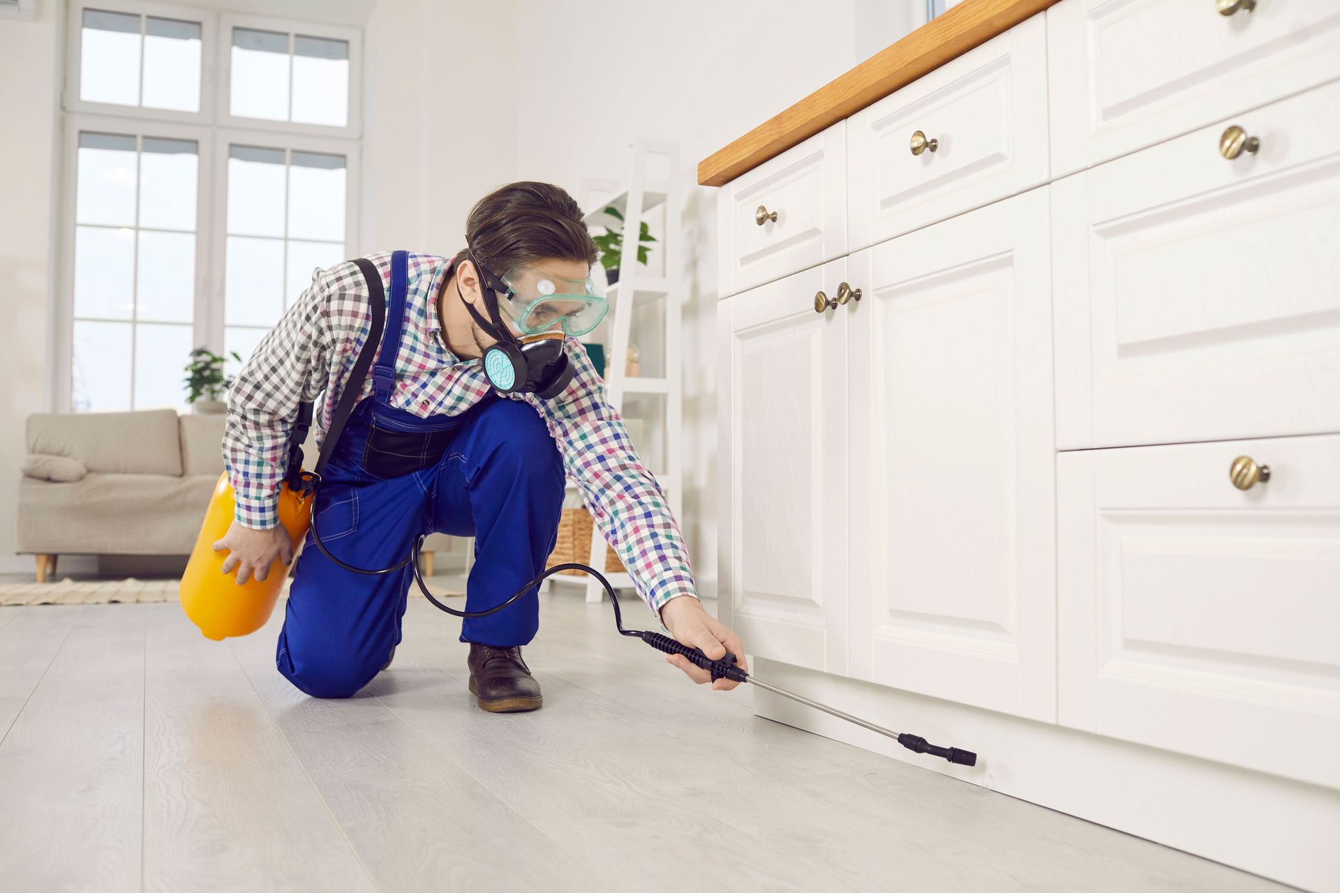 A worker in a mask is performing emergency pest control service, spraying insecticide in the house.