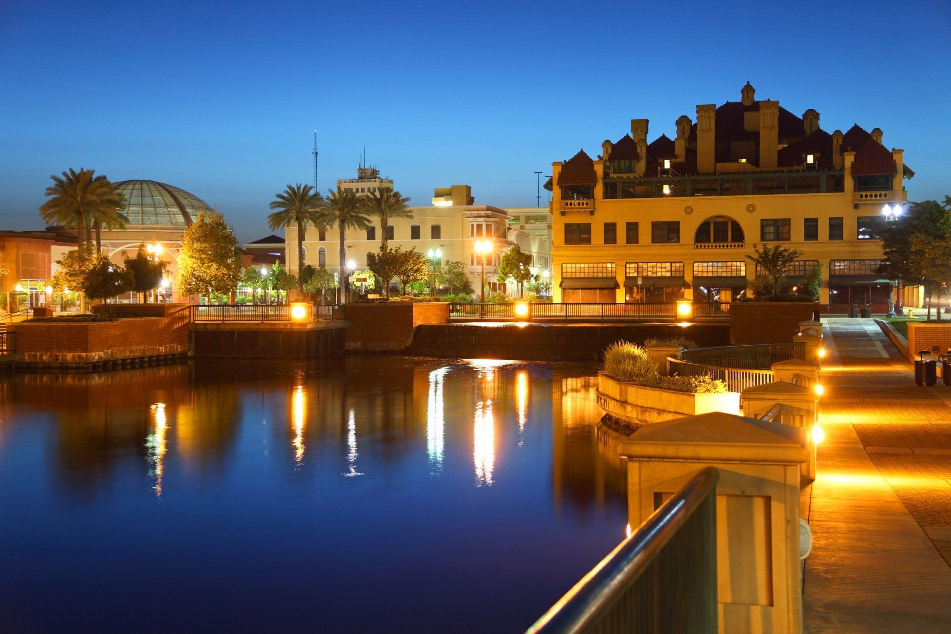 Night view of a city waterfront with buildings and their reflections in the water. Lights are illuminated.