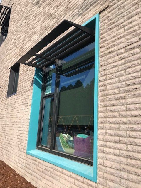 Window with black awning, turquoise frame, and reflective glass in a brick building.