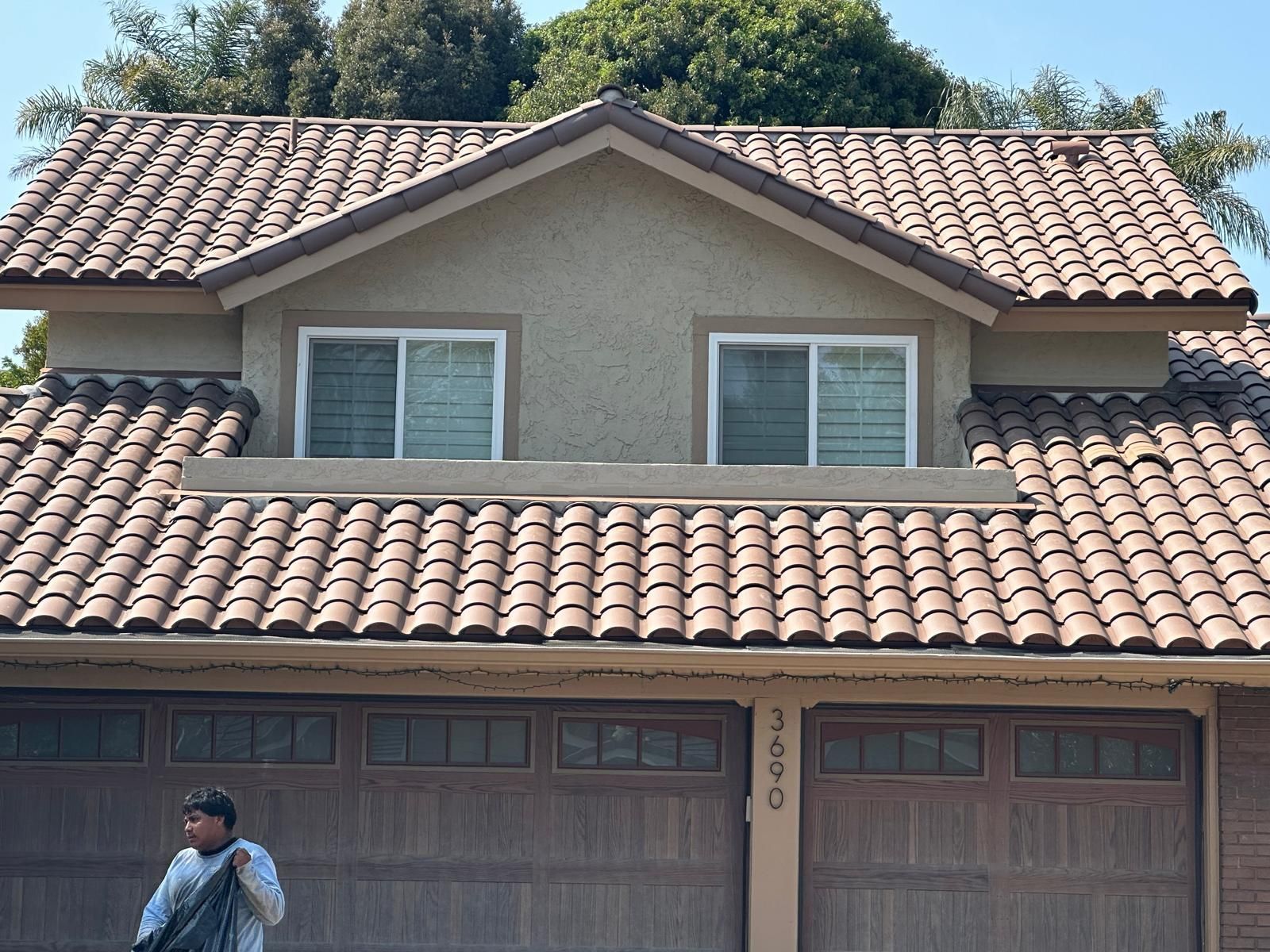 A man is standing in front of a house with a tiled roof.