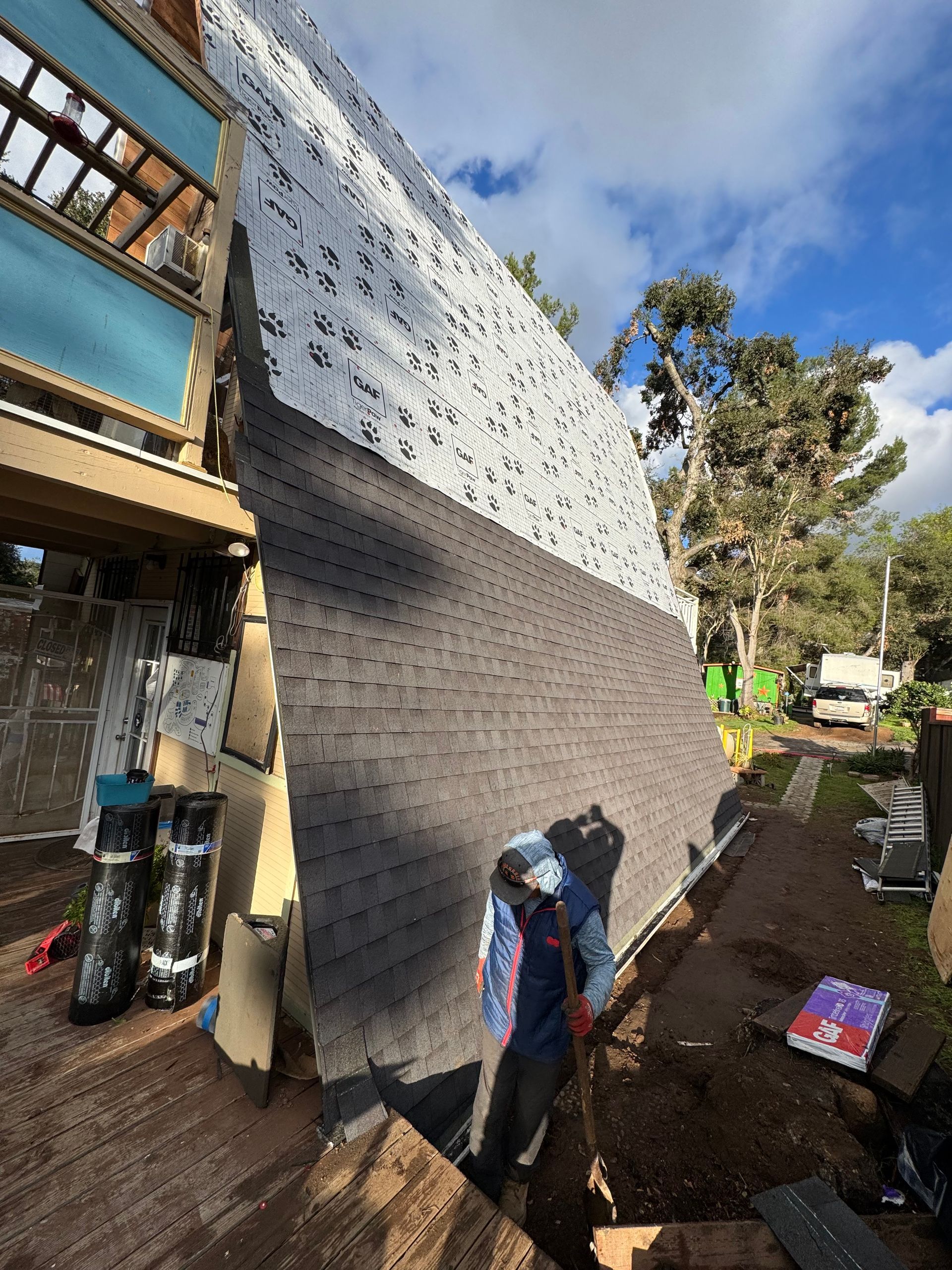 Man working on a roof with gray shingles. New roof construction on a residential building. Blue sky.