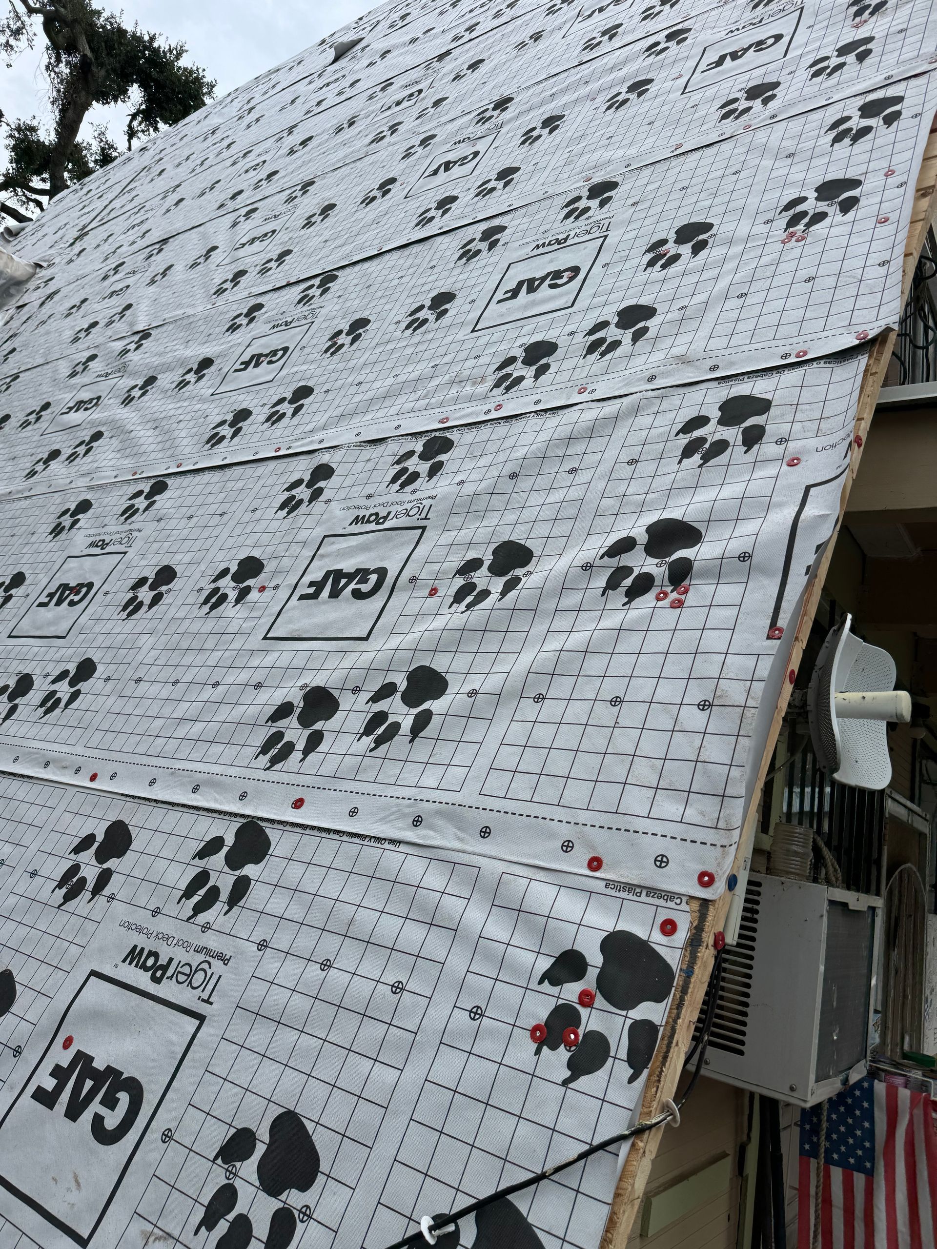 Roof partially covered with GAF roofing underlayment, showing paw print pattern.
